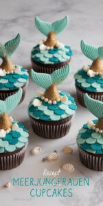 Sechs Meerjungfrauen-Cupcakes auf weißem Marmor – türkis-blaues Schuppen-Muster-Frosting in überlappenden Halbkreisen goldene Fondant-Flossen ragen nach oben Perlmutt-Perlen und Muschel-Dekor